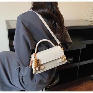 Detailed view of a beige leather crossbody bag with wooden bead charm on a black shelf