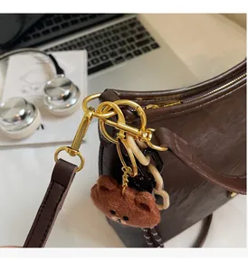 Detail of dark brown leather shoulder bag with golden hardware and plush bear charm