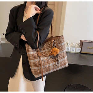 Detail of checkered woolen tote bag with leather straps and teddy bear charm on model