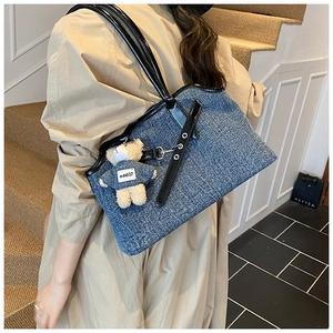 Blue denim tote bag with black leather straps and a cute plush bear charm on stairs