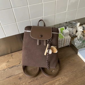 Dettaglio zaino vintage in pelle scamosciata marrone con ciondoli da baseball su tavolo
