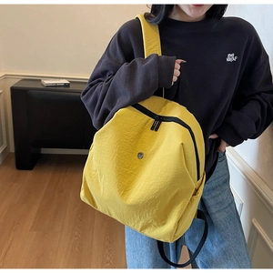 Dettaglio dello zaino in nylon giallo con spallacci neri e logo metallico circolare