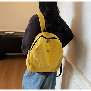 Dettaglio di uno zaino in nylon giallo con doppie cerniere nere e logo in metallo