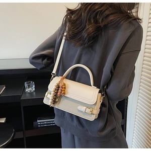 Detail view of cream crossbody bag with wooden bead charm worn by a model in a cafe