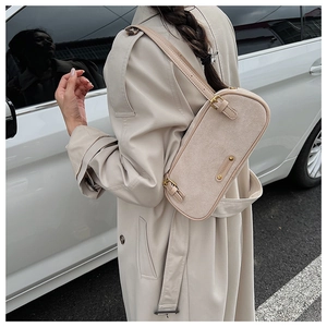 Outdoor view of beige suede shoulder bag with metal buckles on a stylish trench coat