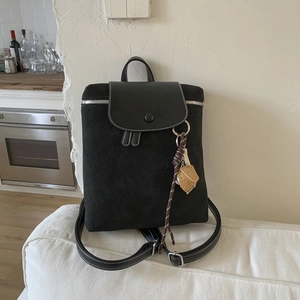 Dettaglio zaino nero opaco con cuciture bianche e ciondolo a guanto da baseball sul divano