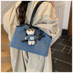 Detail of blue denim tote bag with leather trim and cute teddy bear charm accessory