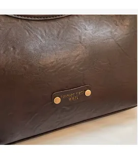 Detailed view of dark brown faux leather texture with vintage gold metal logo plate