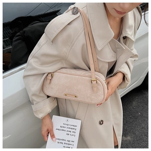 Detalle de bolso cilíndrico de ante beige con correa fina y accesorios de metal dorado