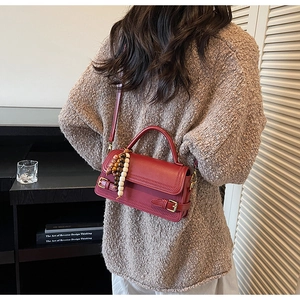 Detail of red vintage crossbody bag with wood bead charm and twin buckle straps