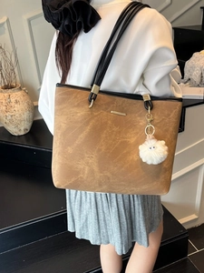 Brown suede tote bag with black straps and plush charm, shown carried on the shoulder