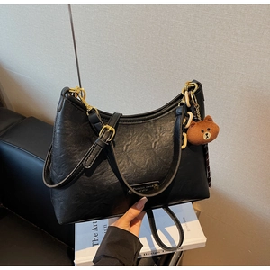 Detail of black faux leather dumpling bag with golden buckle and cute bear charm