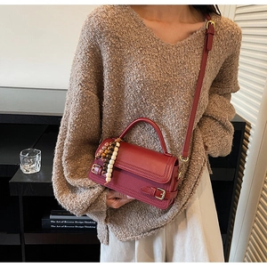 Detail of burgundy vintage crossbody bag with wooden bead charm and matte leather texture