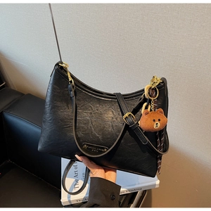 Close-up of black litchi pattern leather shoulder bag with gold logo and bear charm