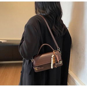 Close-up of a vintage dark brown leather crossbody bag with decorative colorful beads charm