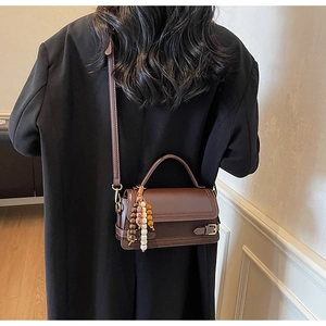 Close-up of vintage brown leather handbag with bohemian beaded charm on black wool coat