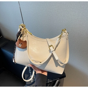 Detail of cream crescent hobo bag with teddy bear charm and gold metal hardware