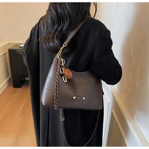 Detail of vintage brown leather handbag featuring a fashion trend metal plaque and plush charm