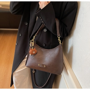 Detail of dark brown leather crescent bag with adjustable strap and bear charm
