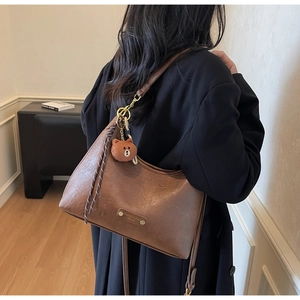 Close-up of brown crescent bag with plush bear charm and chain detail on coat