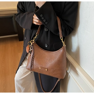 Detail shot of brown vintage PU leather dumpling bag with plush bear charm and woven cord