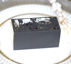 Detail of laser-cut black Halloween candy box with pumpkin and cat motifs on gold background