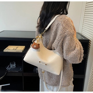 Chic white pleated crescent bag shown on model with cute brown bear charm detail