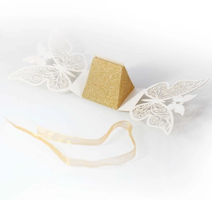Macro shot of laser-cut butterfly wedding favor box with gold glitter inner and silk ribbon