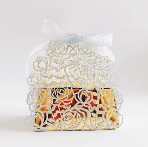 Detail of laser-cut rose pattern wedding favor box with glitter finish and white ribbon
