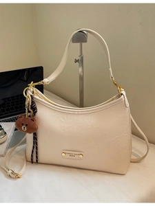 Minimalist beige crescent shoulder bag with a brown bear pendant and metal logo plate