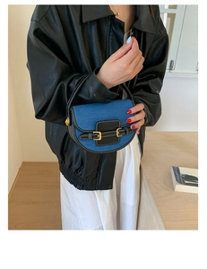 Detail of denim and black leather saddle bag with gold buckles and white stitching