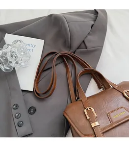 Detail of a brown PU leather bag with gold buckle and embossed brand on a grey blazer