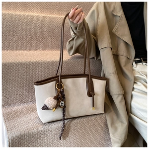Detail view of contrast color tote bag with plush ball charm and leather shoulder straps