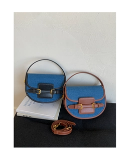 Detail view of denim saddle bag with premium leather trim and metal buckle closure