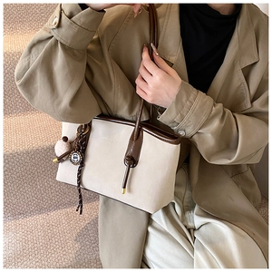 Detail of beige suede tote bag with brown leather trim and metal charm on a model