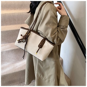 Detail of a large tote bag with brown leather trim and decorative plush pendant accessory