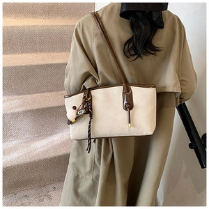 Detail of a minimalist cream tote bag with brown leather handles and a fuzzy pom-pom charm