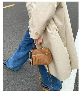 Détail d'un sac bandoulière en daim marron avec fermetures argentées et pendentif tressé