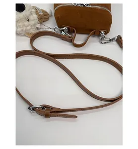 Detail of adjustable strap and plush puppy charm on a brown suede crossbody bucket bag