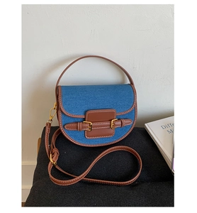 Detail of blue denim and brown leather patchwork saddle bag with dual metal buckles