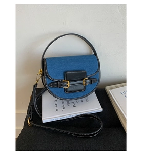 Detailed close-up of denim saddle bag with black leather trim and contrast white stitching
