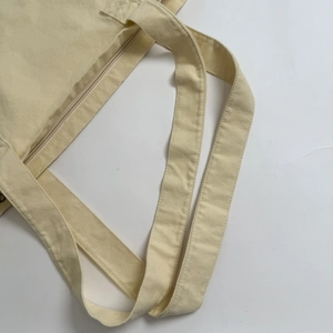 Detail of cream canvas tote bag showing reinforced straps and top zipper closure