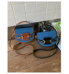 Detail of denim saddle bags with brown and black leather trim on a wooden tabletop