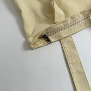 Detail of zip closure and reinforced stitching on beige canvas tote bag shoulder straps