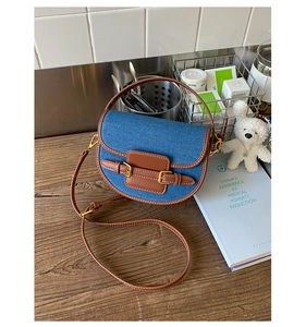 Detail of a vintage denim saddle bag with brown leather trim and golden metal buckles