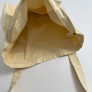 Spacious beige canvas tote bag with zipper closure and reinforced interior pocket view