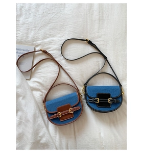 Top view of two denim saddle bags with brown and black leather trim on white fabric