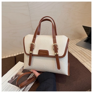 Detail of white textured leather handbag with brown straps and golden metal buckles