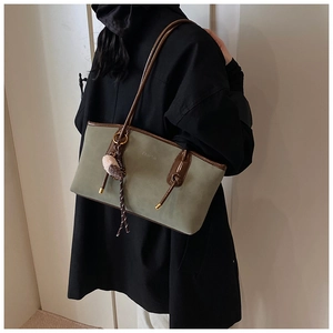 Detail view of large sage green suede tote bag with brown leather straps and plush charm