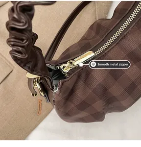 Detail shot of smooth gold-tone zipper and coffee plaid texture on the handbag